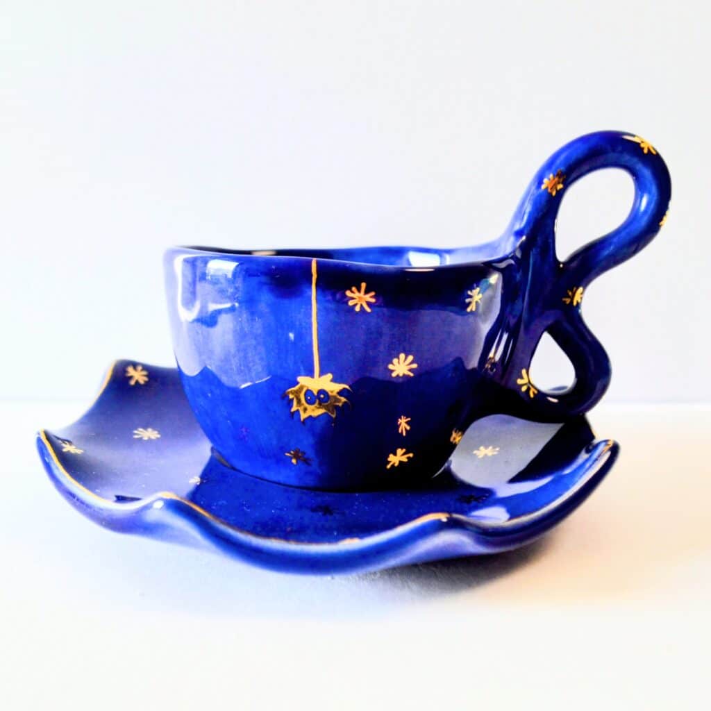 Handmade dark blue ceramic mug with a base, yellow spider motif and stars.