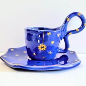Handmade dark blue ceramic mug with a base, yellow spider motif and stars.