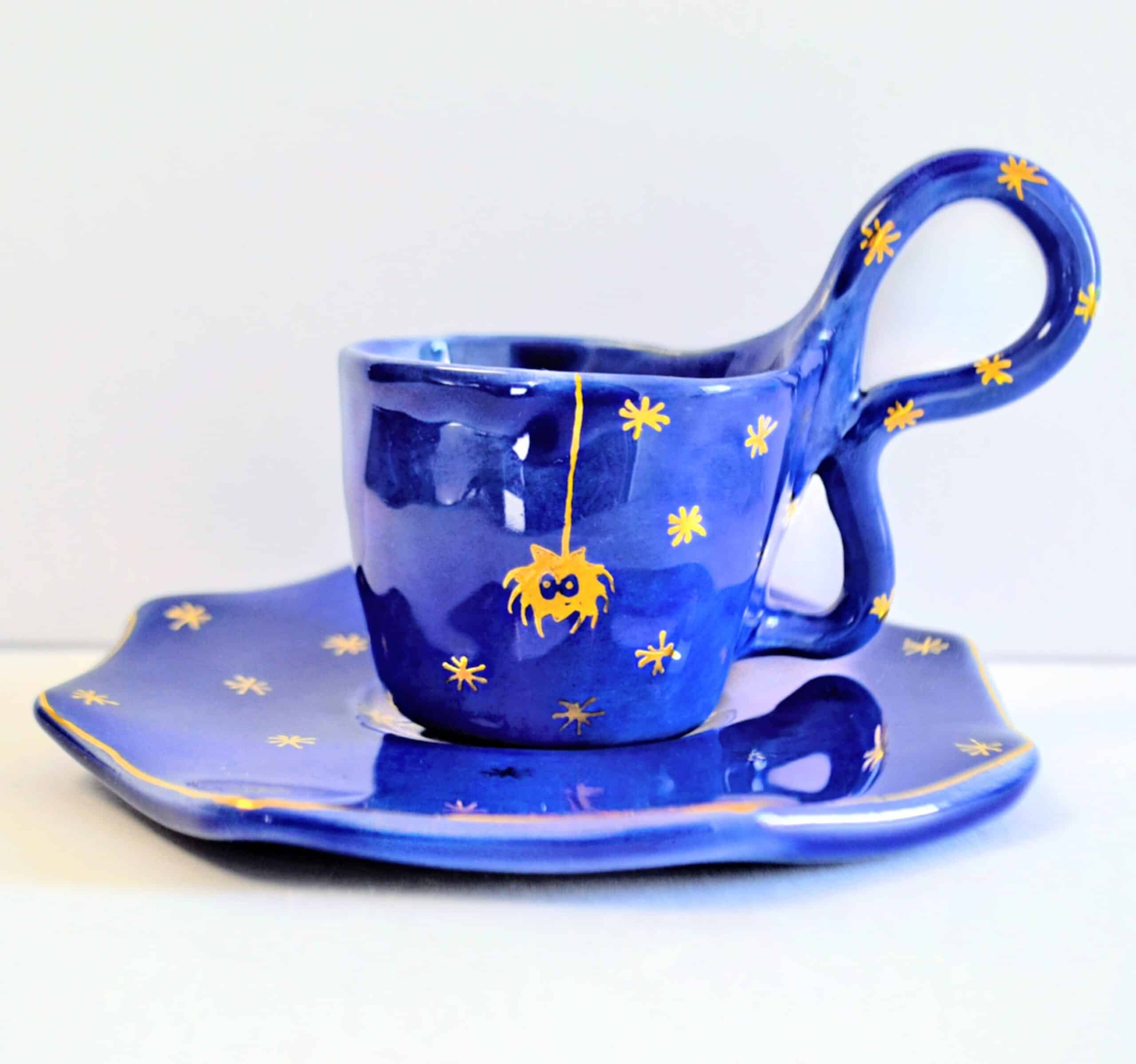 Handmade dark blue ceramic mug with a base, yellow spider motif and stars.