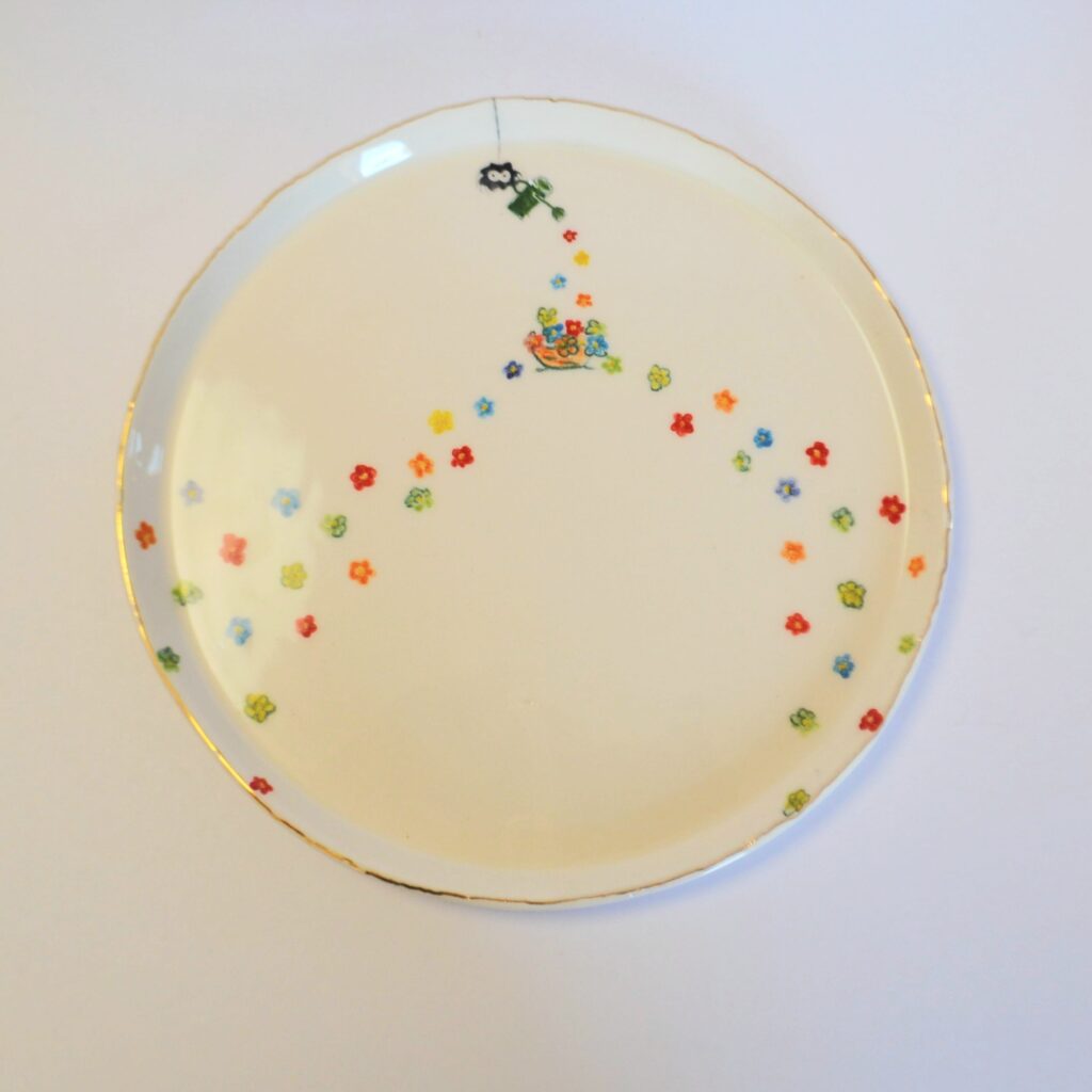 Dish with gold rim, painted spider watering tiny colorful flowers.