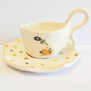 Handcrafted white stoneware cup with a unique organic handle, featuring a hand-painted spider watering tiny colorful flowers.