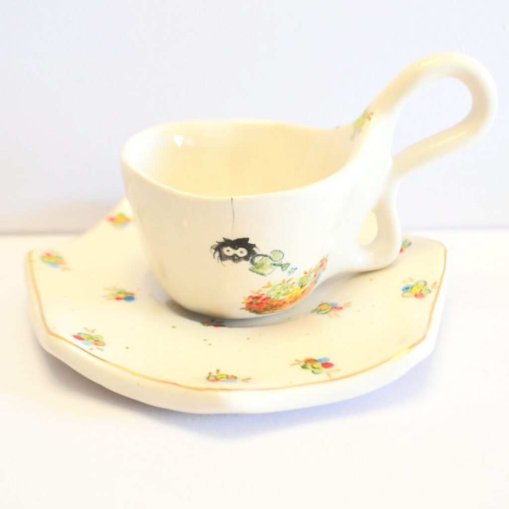 Front of mug and soucer. Hand-painted spider watering tiny colorful flowers.