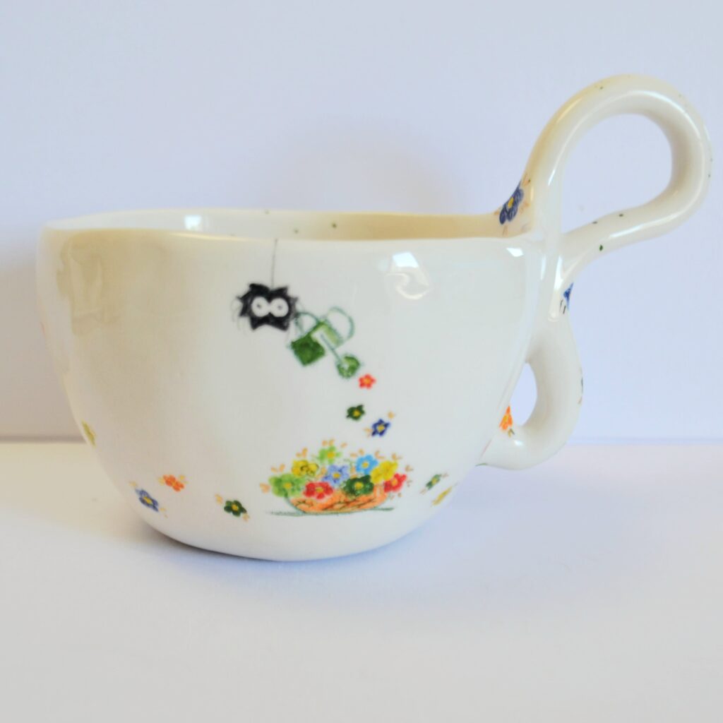 Handcrafted white stoneware cup with a unique organic handle, featuring a hand-painted spider watering tiny colorful flowers.